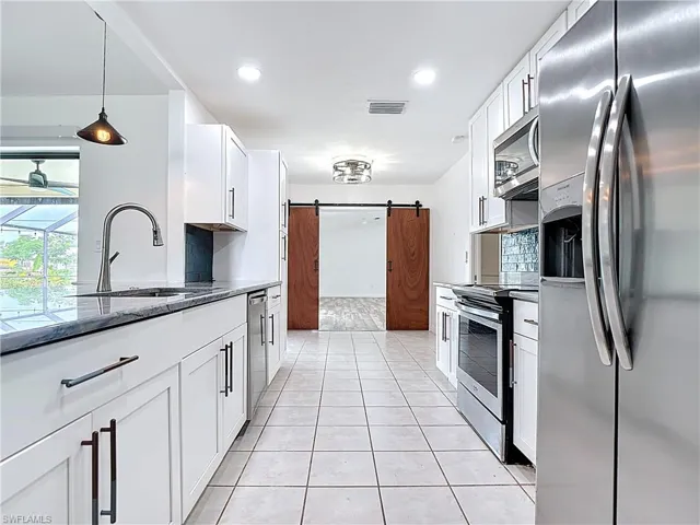Kitchen featuring stainless steel appliances, a barn door, dark stone counters, white cabinetry, and light tile patterned floors