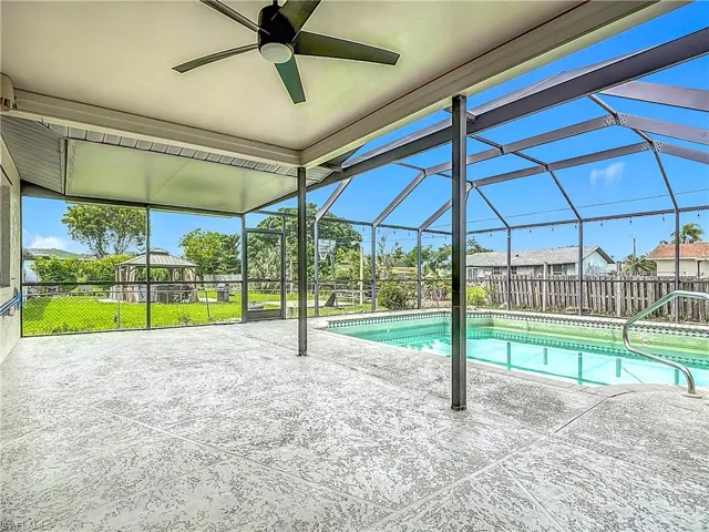 View of pool featuring a patio area, a ceiling fan, a fenced backyard, and glass enclosure