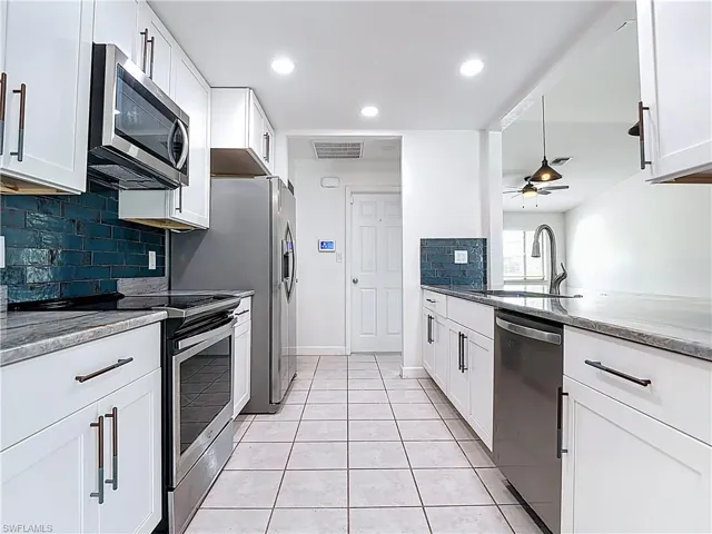 Kitchen featuring appliances with stainless steel finishes, backsplash, a ceiling fan, white cabinets, and light tile patterned flooring
