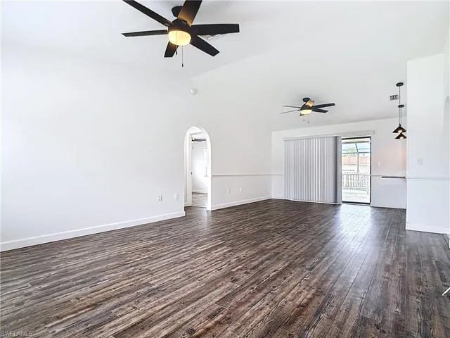 Unfurnished living room featuring a ceiling fan, dark wood-style flooring, vaulted ceiling, and arched walkways