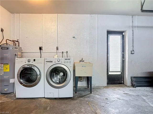 Laundry room featuring water heater, washing machine and clothes dryer, and a textured wall