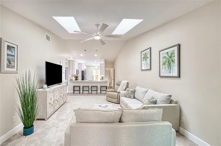 Living room with a skylight, lofted ceiling, light carpet, and baseboards