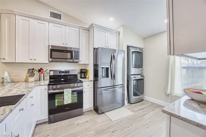 Kitchen featuring appliances with stainless steel finishes, stacked washing machine and dryer, lofted ceiling, light wood-style floors, and baseboards