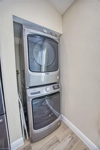 Laundry area with stacked washer / dryer, wood finish floors, baseboards, and a textured wall