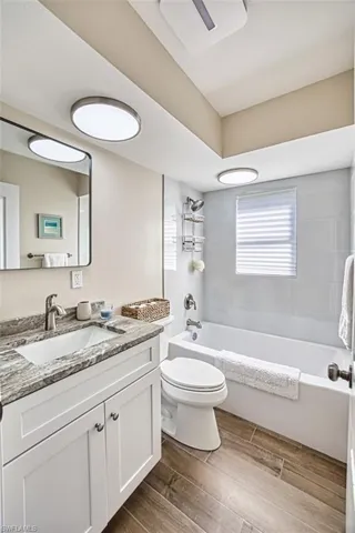 Bathroom with toilet, wood finished floors, vanity, and shower / washtub combination