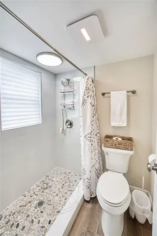 Bathroom featuring wood finished floors, toilet, and tiled shower