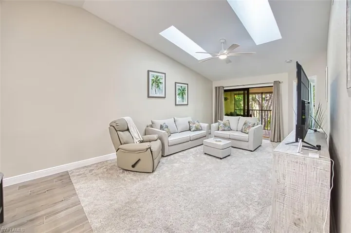 Living area featuring a skylight, lofted ceiling, light wood-style flooring, baseboards, and ceiling fan