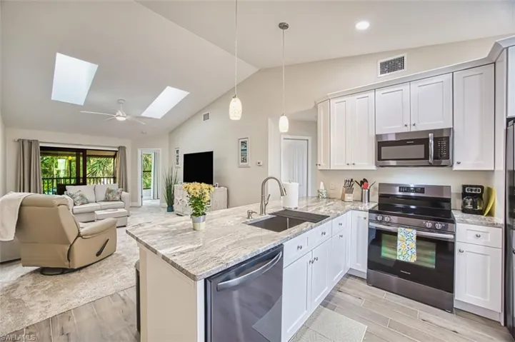 Kitchen featuring appliances with stainless steel finishes, a sink, a skylight, a peninsula, and vaulted ceiling