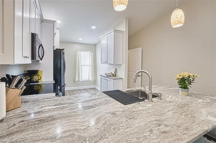 Kitchen featuring black appliances, light stone countertops, light wood finished floors, white cabinetry, and decorative light fixtures