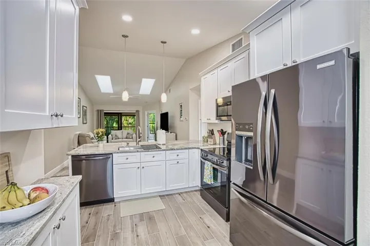 Kitchen with stainless steel appliances, a skylight, a sink, open floor plan, and vaulted ceiling