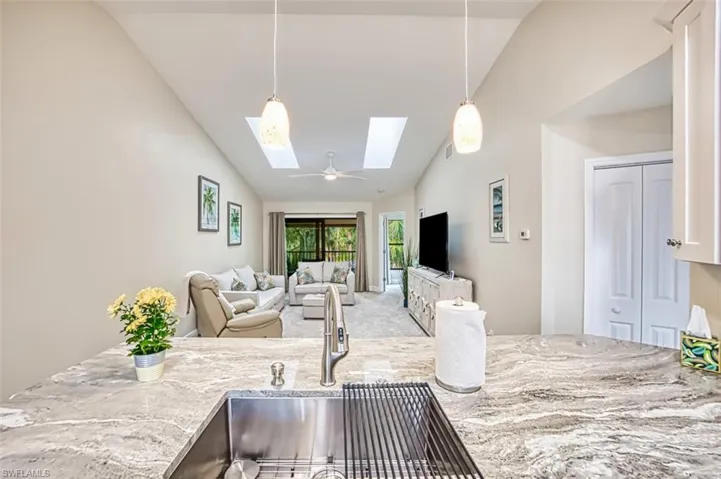 Kitchen featuring vaulted ceiling, a skylight, light stone countertops, a sink, and decorative light fixtures