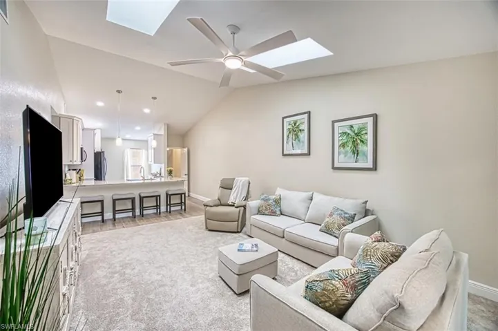 Living area with a skylight, vaulted ceiling, baseboards, a ceiling fan, and light wood-type flooring