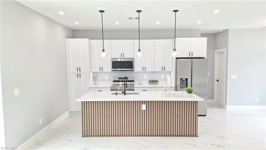 Kitchen with stainless steel appliances, a center island with sink, white cabinetry, light stone counters, and pendant lighting