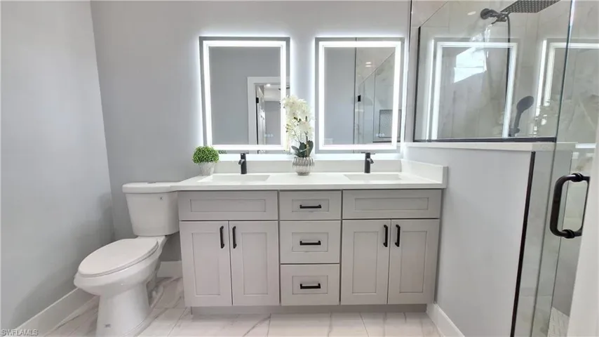 Full bath with double vanity, a shower stall, and light marble finish floors