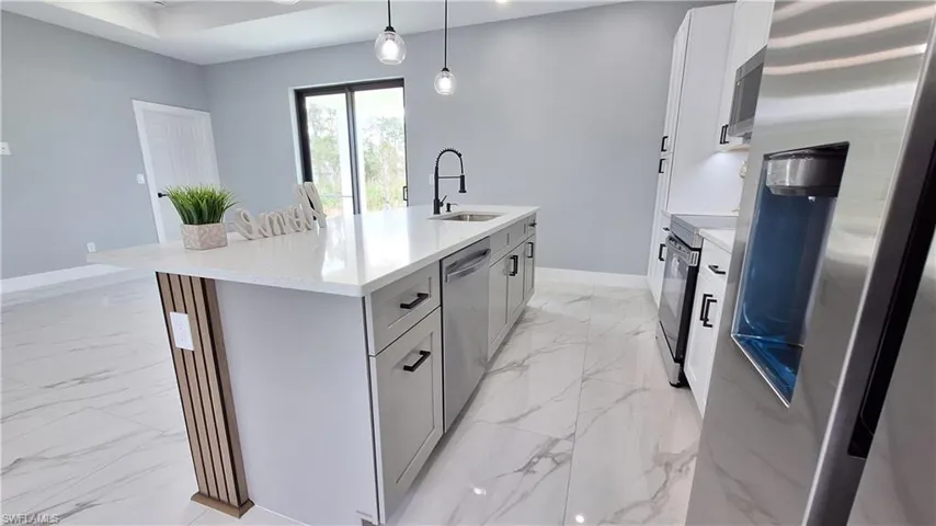 Kitchen with stainless steel appliances, a kitchen island with sink, light marble finish flooring, light stone countertops, and decorative light fixtures