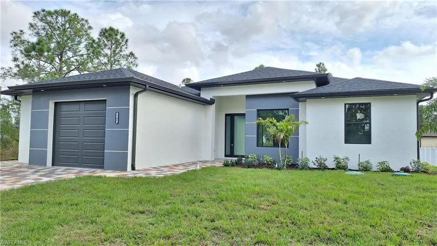 View of front facade featuring a front lawn, stucco siding, an attached garage, and roof with shingles