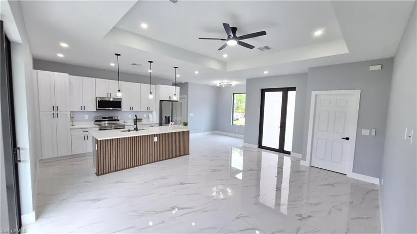 Kitchen with open floor plan, an island with sink, white cabinets, ceiling fan, and a tray ceiling