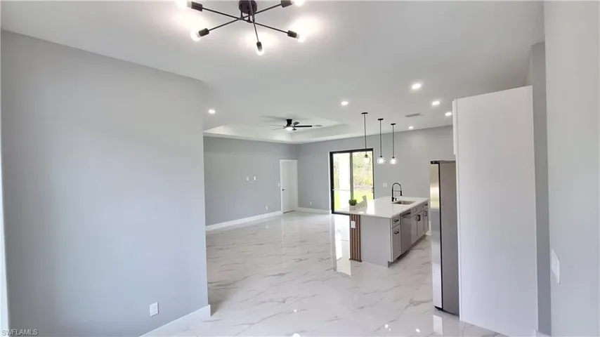 Kitchen featuring open floor plan, an island with sink, stainless steel appliances, a tray ceiling, and hanging lights