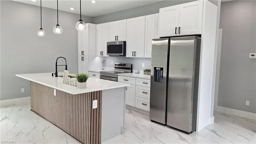 Kitchen featuring stainless steel appliances, an island with sink, light stone countertops, and white cabinetry