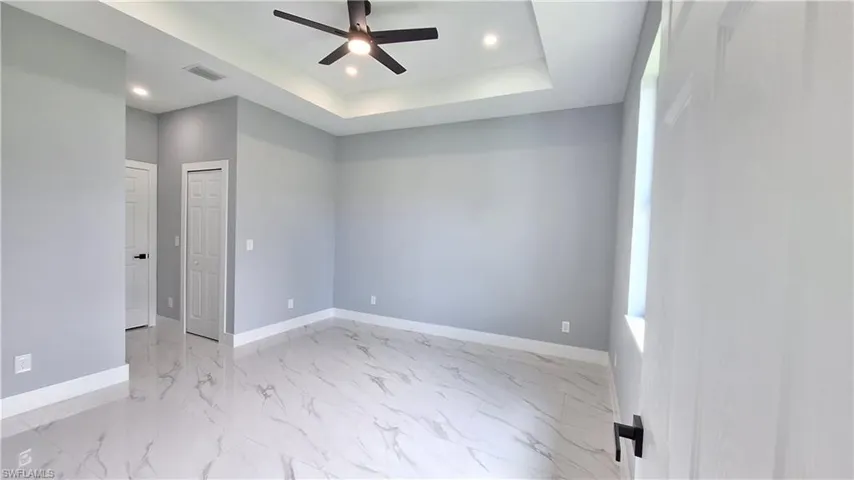 Spare room featuring ceiling fan, a tray ceiling, recessed lighting, and light marble finish flooring