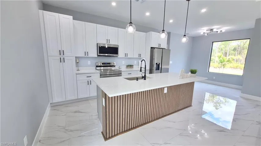 Kitchen with stainless steel appliances, light marble finish floors, white cabinetry, and a center island with sink
