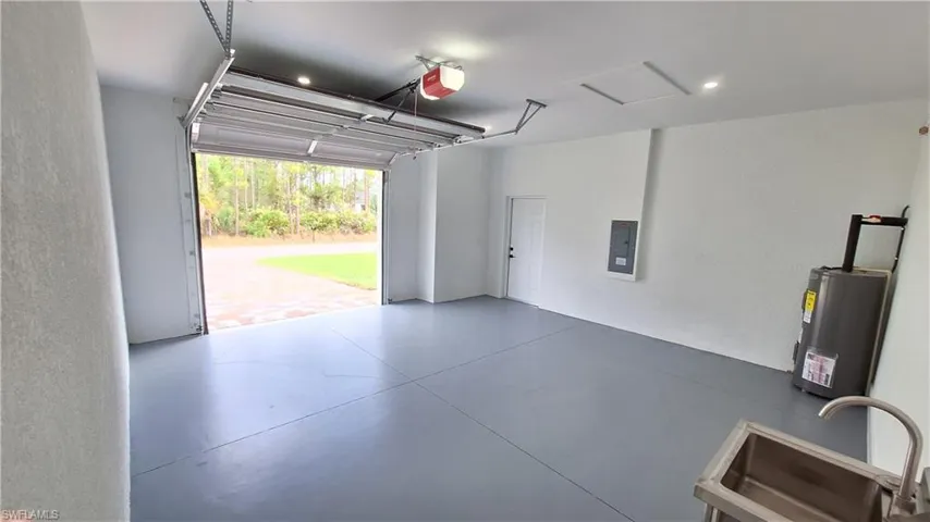 Garage featuring electric water heater, electric panel, a textured wall, and a garage door opener