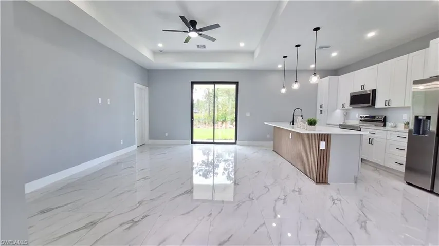Kitchen featuring white cabinetry, stainless steel appliances, open floor plan, an island with sink, and a raised ceiling