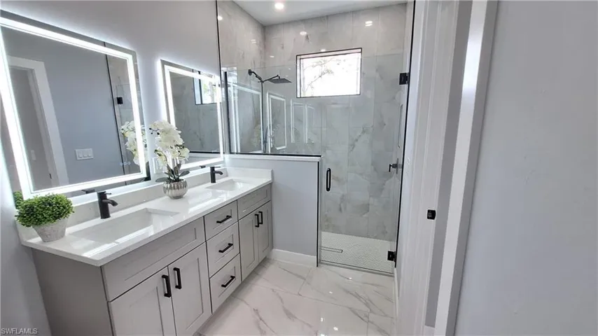 Bathroom with double vanity, a marble finish shower, and light marble finish floors