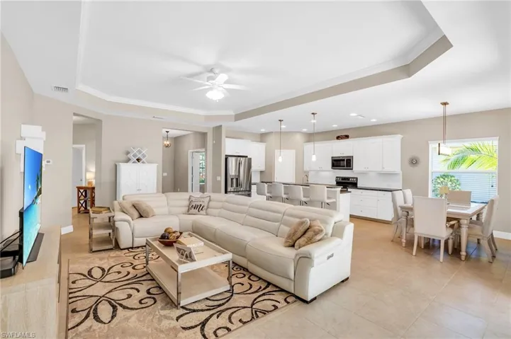 Living room with a ceiling fan, a raised ceiling, crown molding, and light tile patterned flooring
