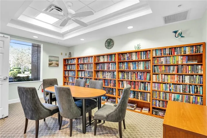 Living area featuring visible vents, a ceiling fan, a tray ceiling, carpet floors, and bookshelves