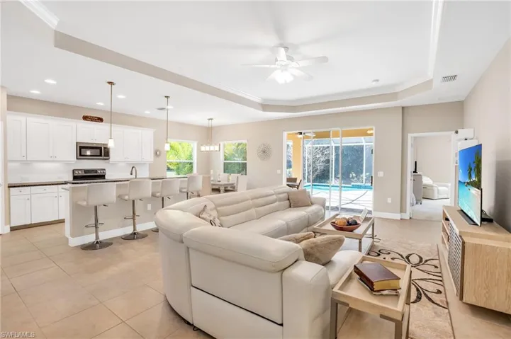 Living area featuring light tile patterned flooring, a ceiling fan, visible vents, baseboards, and a raised ceiling