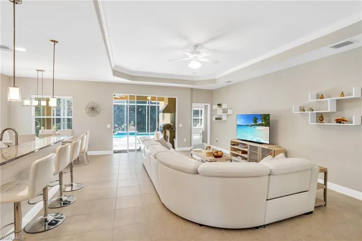 Living area featuring light tile patterned floors, baseboards, a ceiling fan, a tray ceiling, and crown molding