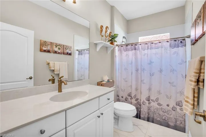 Bathroom with toilet, marble finish floor, a shower with shower curtain, and vanity