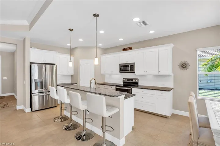 Kitchen with a breakfast bar, visible vents, appliances with stainless steel finishes, white cabinetry, and an island with sink