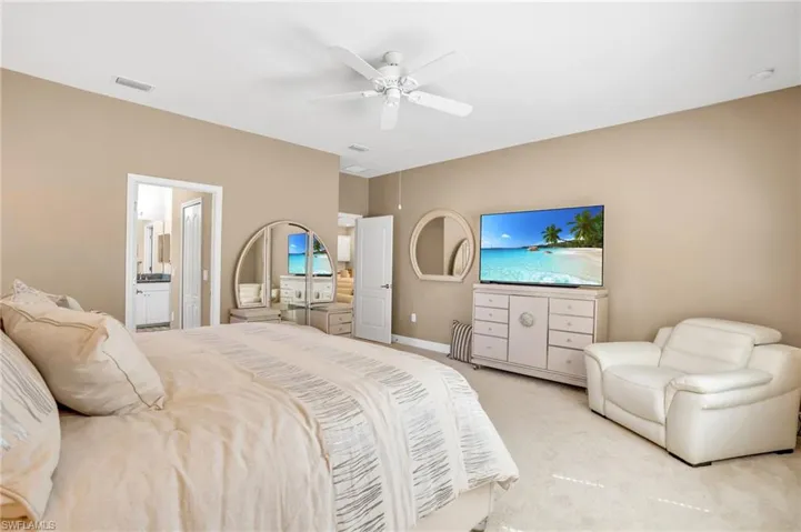 Bedroom featuring light carpet, visible vents, a ceiling fan, baseboards, and ensuite bath