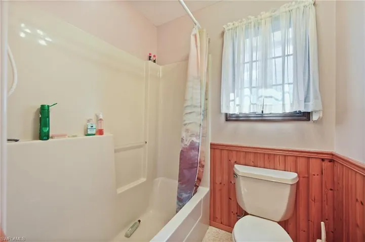 Bathroom featuring wainscoting, shower / bath combo with shower curtain, and wood walls