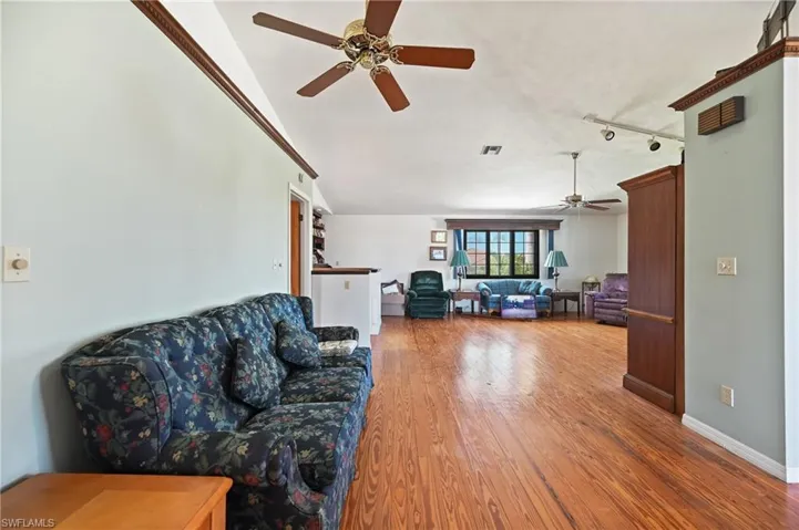 Living area with wood finished floors, a ceiling fan, vaulted ceiling, and track lighting