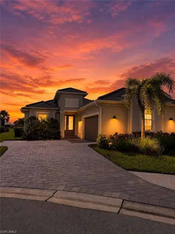 Paved driveway and walkway, exterior wall-mounted lighting, garage, prominent palm tree, and lush landscaping