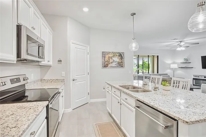 Kitchen featuring white cabinets, stainless steel appliances, a center island with sink, a ceiling fan, and light stone counters
