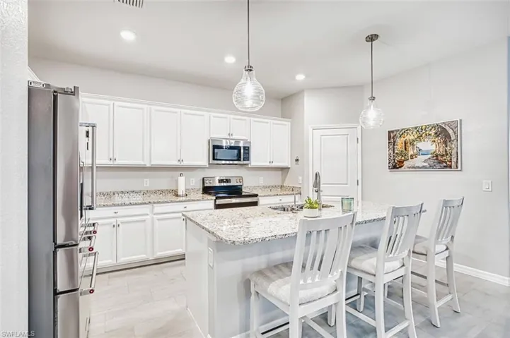 Kitchen with white cabinets, stainless steel appliances, a kitchen bar, and light stone counters