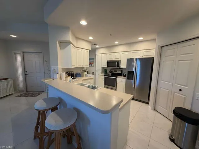 Kitchen with a peninsula, a kitchen breakfast bar, stainless steel appliances, white cabinets, and light countertops