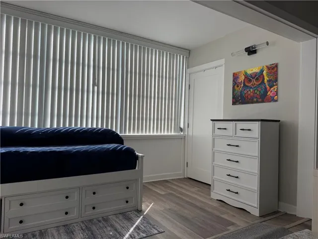 Vertical window blinds, wood-finish flooring, white door, wall-mounted light fixture, and crown molding