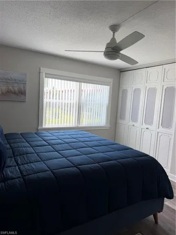 Built-in wardrobe storage, neutral ceiling fan, white window trim, and wood-finish flooring