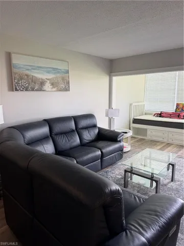 Recessed opening to an additional room, white window blinds, and wood-finish flooring