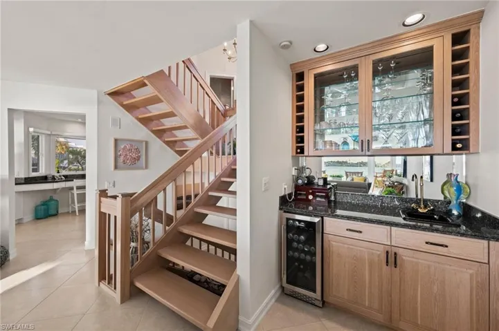Bar with light tile patterned flooring, dark stone countertops, sink, and beverage cooler