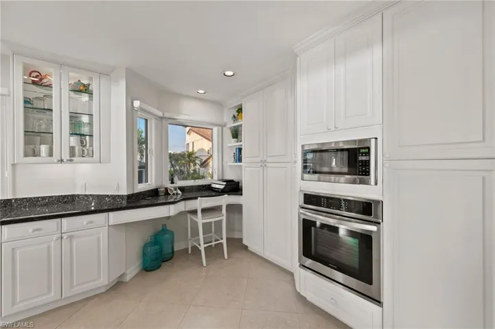 Kitchen with dark stone countertops, white cabinetry, light tile patterned floors, and appliances with stainless steel finishes