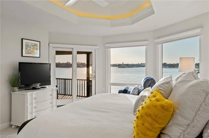 Carpeted bedroom featuring access to exterior, a tray ceiling, ceiling fan, crown molding, and a water view