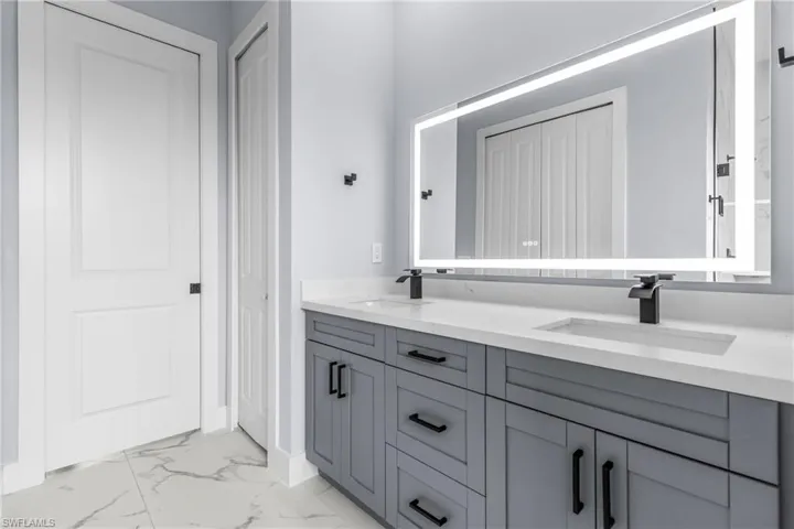 Bathroom featuring light marble finish floors, double vanity, and a closet