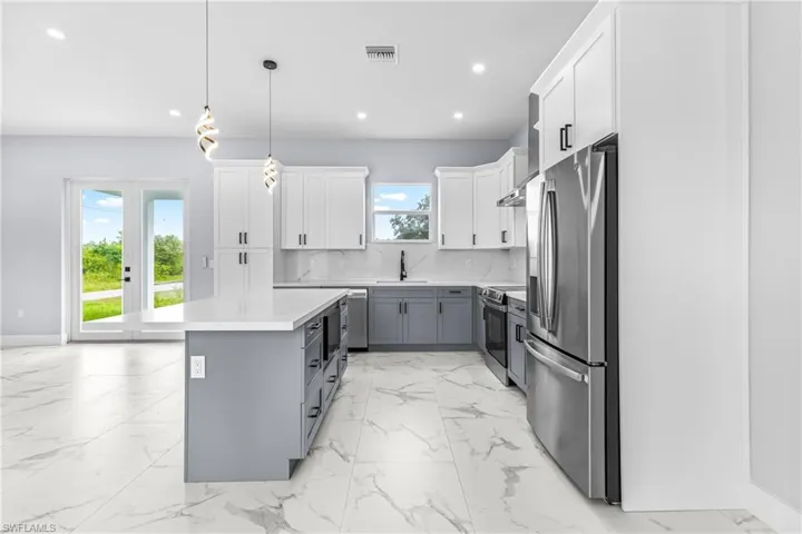 Kitchen with gray cabinetry, white cabinets, appliances with stainless steel finishes, hanging light fixtures, and tasteful backsplash