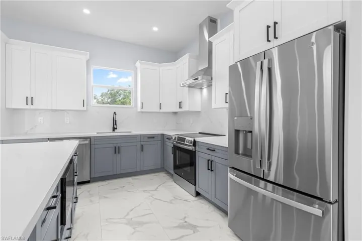 Kitchen with stainless steel appliances, white cabinets, gray cabinetry, backsplash, and light stone countertops